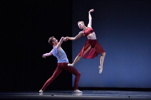 A dancer in red stands on her partner's leg