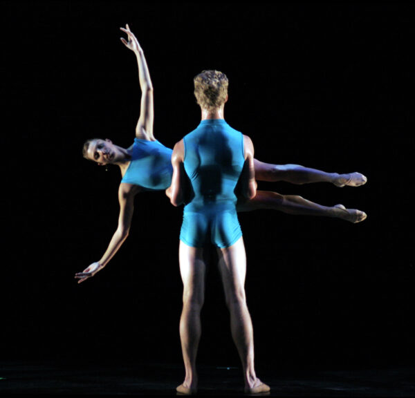 A male dancer in blue lifts a female dancer horizontally