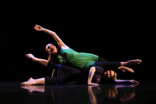 A dancer in green is supported by a dancer on the floor