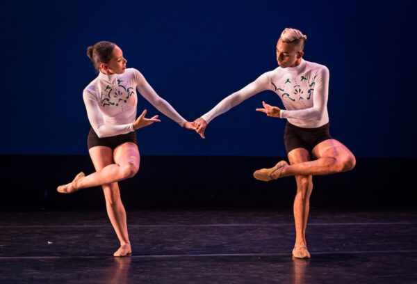 Two dancers hold hands standing on one leg