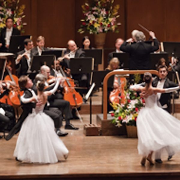 two couples in ballgowns dance before an orchestra