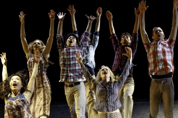 A group of dancers lift their arms and faces