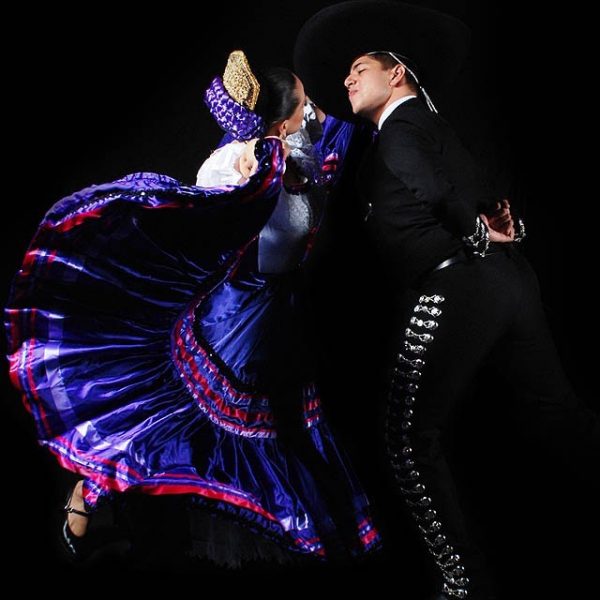 A couple in Mexican folkloric costumes lean toward each other