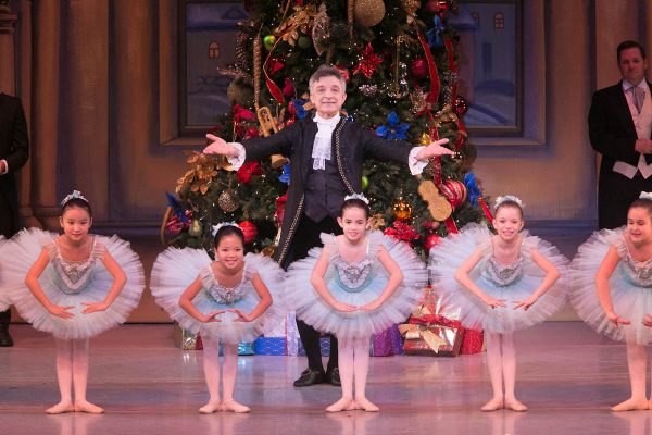 A dressed up man stands behind young ballet dancers