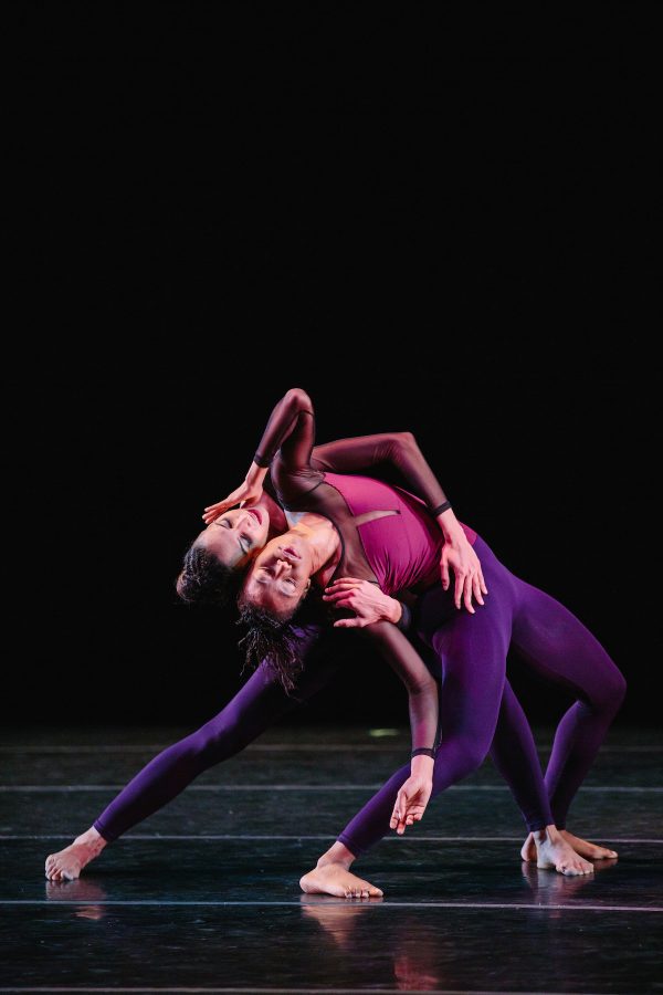 Two dancers in purple tights bend backwards