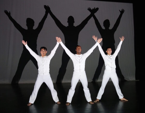 Three men in white lift their arms