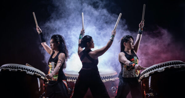 Three female drummers against a smokey background