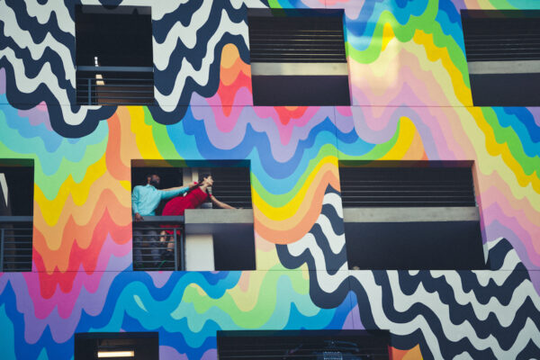 Two dancers lean out of a technicolor building