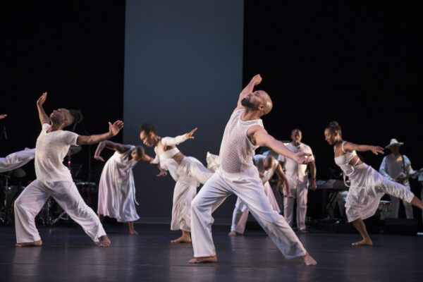 A group of dancers in white fill a stage