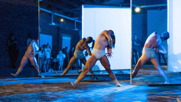 Dancers in white trunks stand in front of white panels
