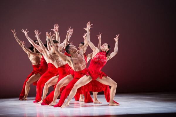 A group of dancers in red lift their arms