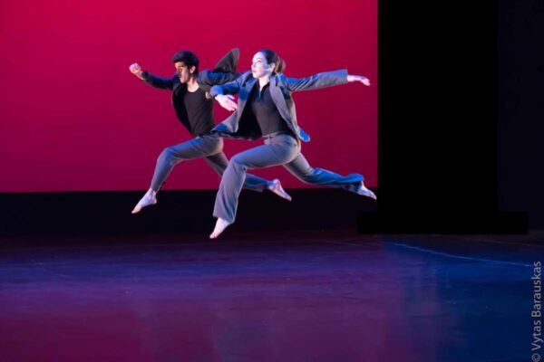 Two dancers in blue suits leap in the air