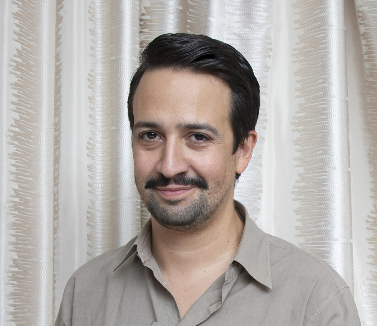It's Lin-Manuel Miranda again, this time in a light gray button down, his hair combed all nicely, his classic smirk on his face.