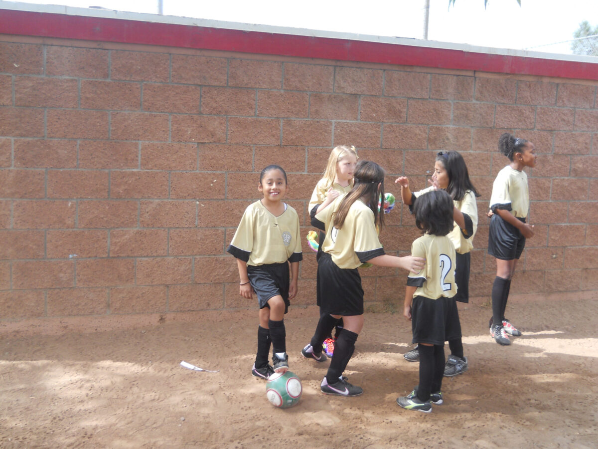 a group of six girls enjoying being around each other in their gold soccer uniforms.