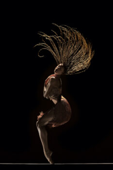 A tall dancer in shadow flips long braids