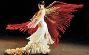 Flamenco dancer in white swirls a red fringed scarf