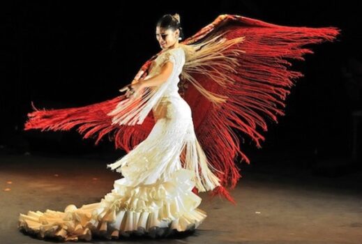 Flamenco dancer in white swirls a red fringed scarf