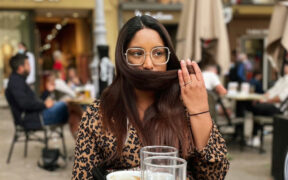 A beautiful Brown woman, masked up and out, at a cafe.
