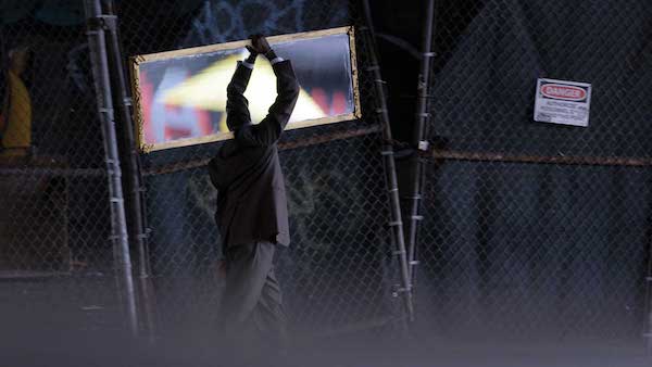 A man holding his arms above his head dances in front of a chain link fence.