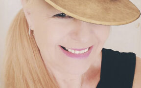 An older blond woman wearing a hat and smiling