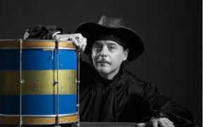Poet Rich Ferguson waers a black hat and is seated next to a drum (blue and gold).