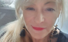 Poet Mish Murphy, an o lder woman with blond hair, earrings, red lipstick, small smile