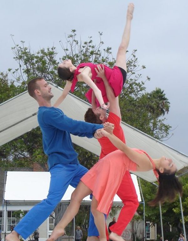 Two men hold a woman in the air while holding another woman in a backbend
