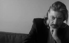 This is a black and white photo of poet Mark Murphy; a man in a dark suit rests his head on his hand, looking thoughtful.