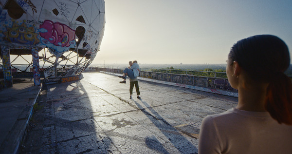 A woman watches a man carrying a woman near a large spherical structure