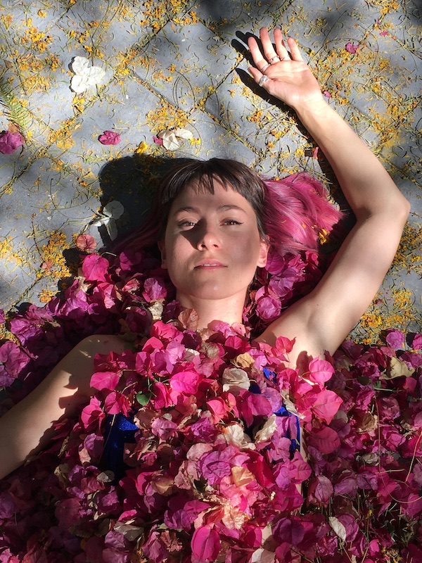 A young woman lies covered with dark pink flowers
