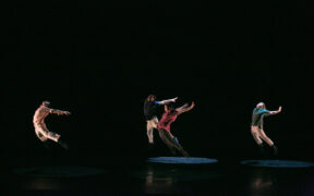 Four figures dance against a black background
