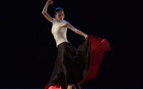 A dancer in a white top, black skirt and red underskirt