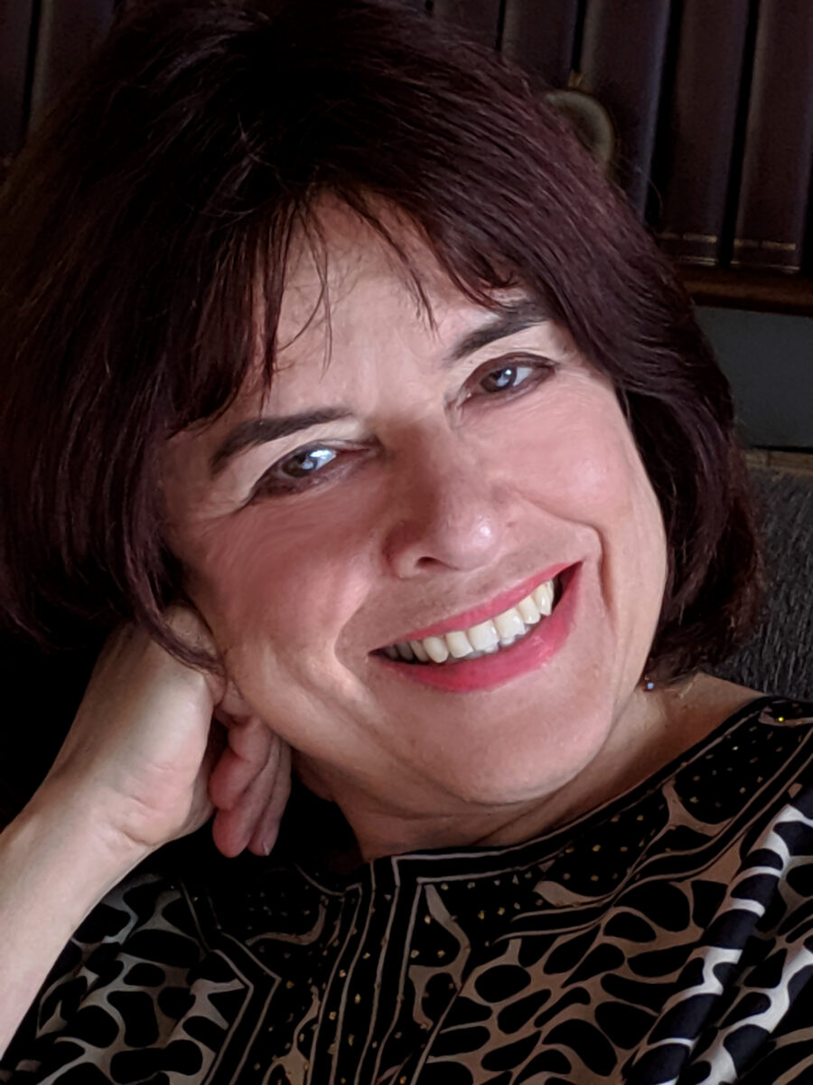 A close-up photo of Columbian poet and translator Ximena Gómez. She's smiling at the camera, her right hand rest on the right side of her face, she's smiling directly at the camera. Hair is short reddish brown. 