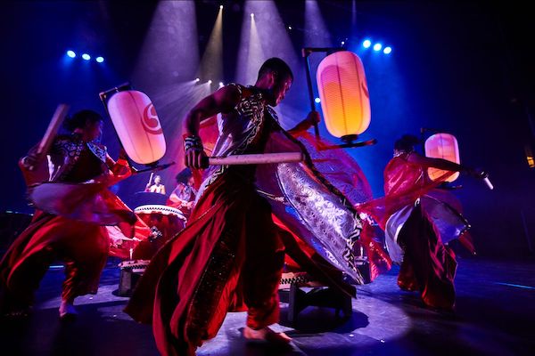 Taiko drummers move under glowing lanterns