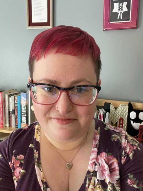 Headshot of poet Marisa Siegel. She has short red hair on top, short brown hair on side, with large rimmed glasses and possibly a nose ring. She stares directly at the camera.