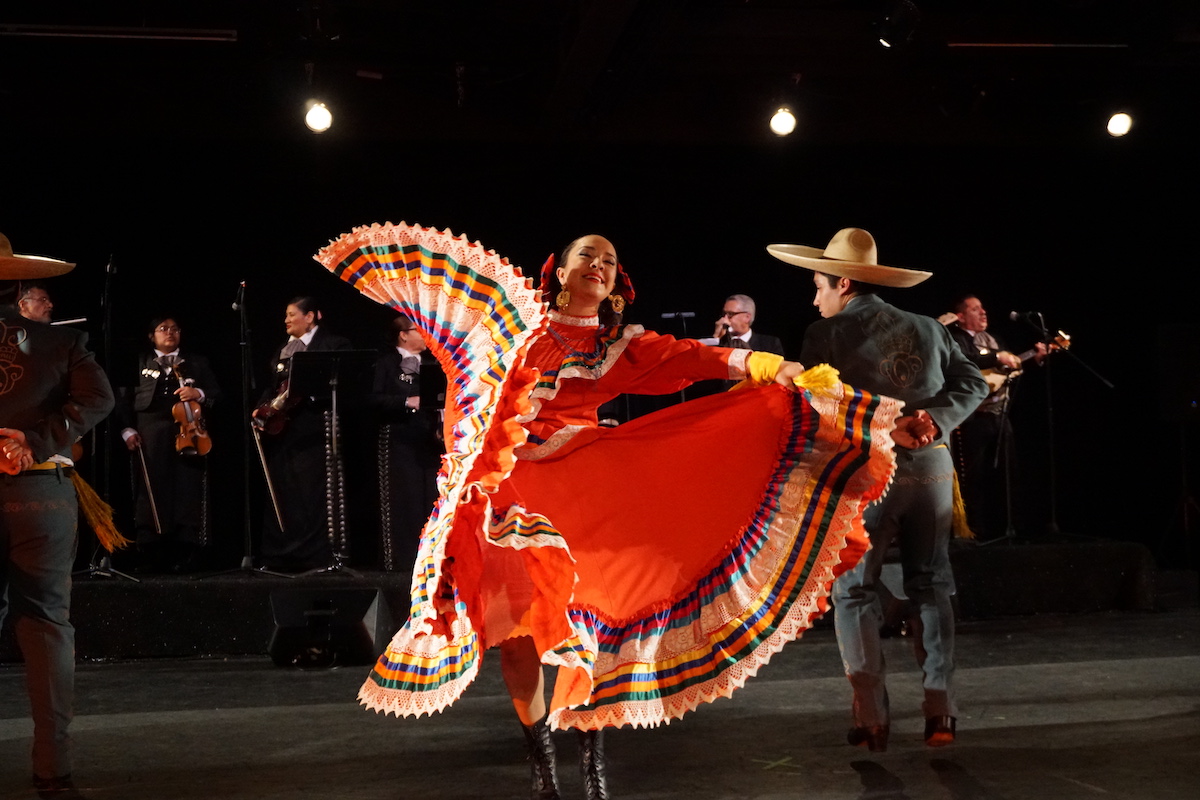 A folkloric dancer in bright orange skirt dances with a man in sombrero