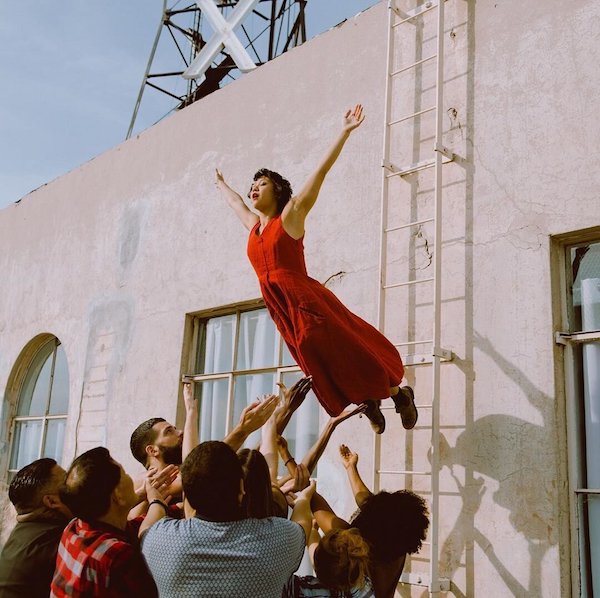 A woman in a red dress leaps off of a ladder