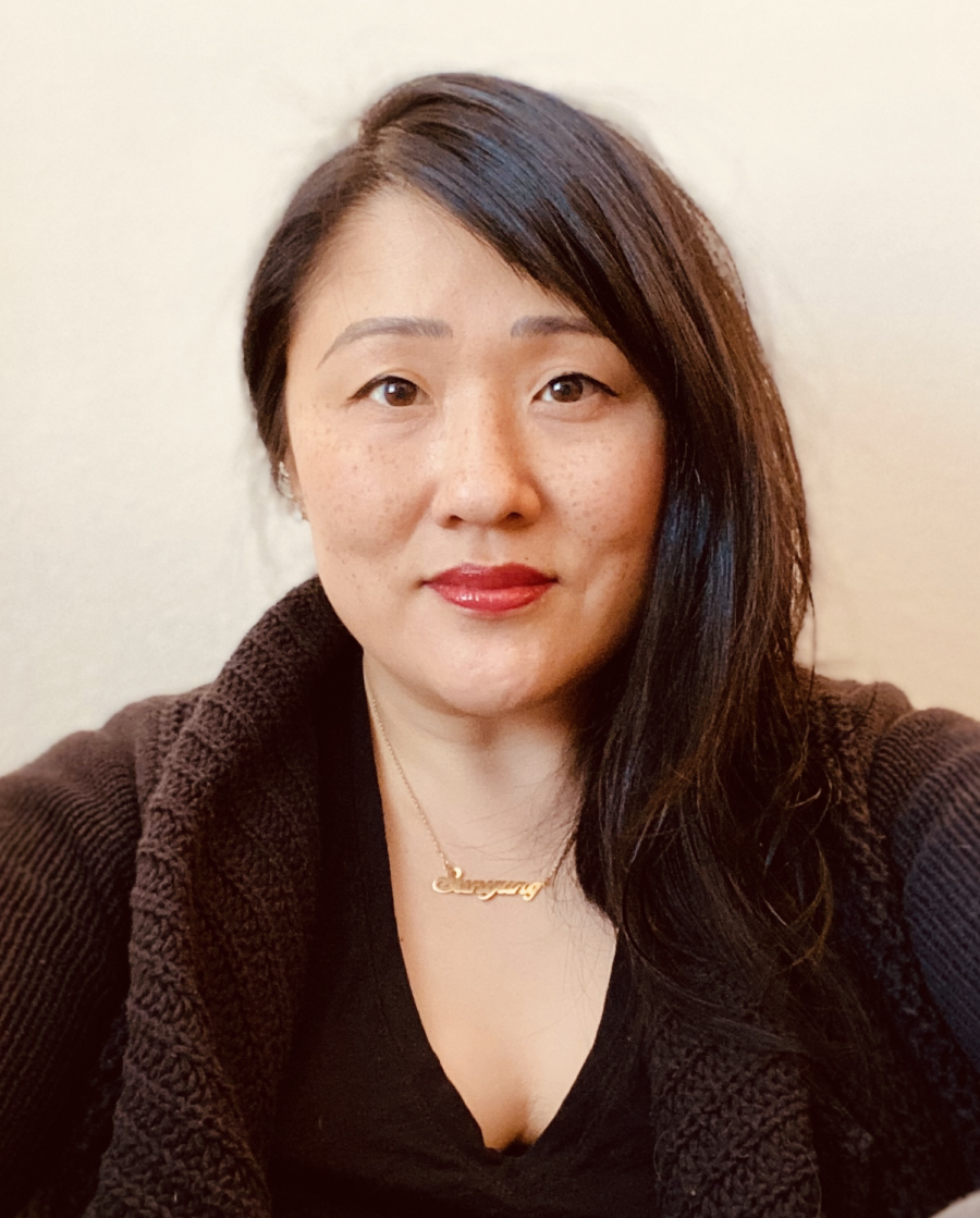 Color photo of Korean-American poet Sun Yung Shin. She has long black hair combed to her left. She looks directly at her camera; she's smiling.