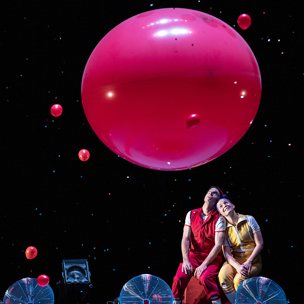 Two dancers stare at a large red balloon