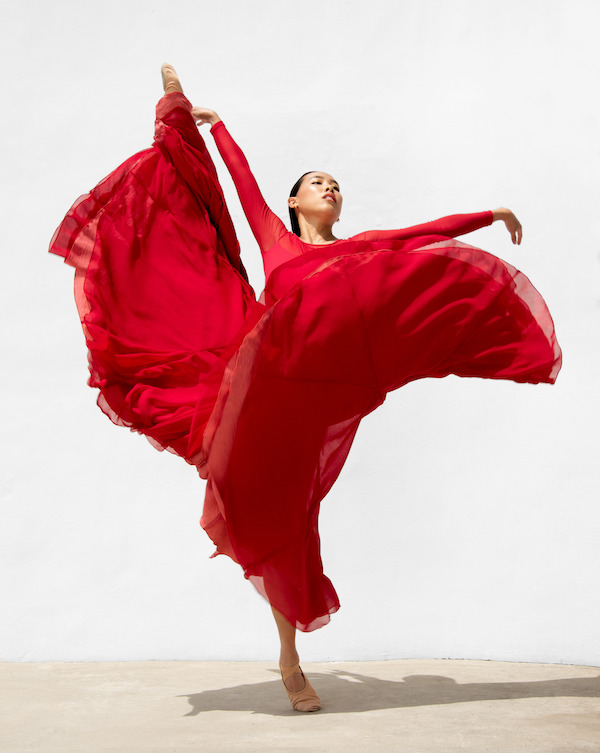 A woman in a long red skirt lifts her leg