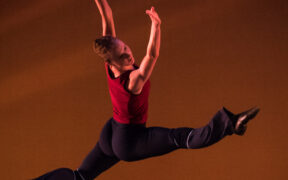 A dancer in a red shirt leaps in the air