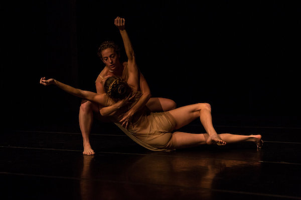 A dancer holds another dancer on floor with outstretched arms