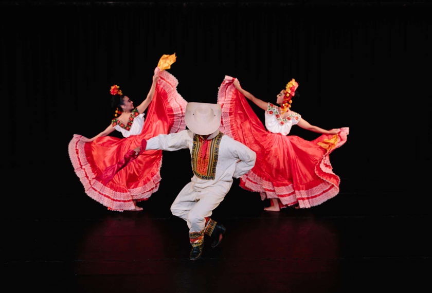 Two folkloric dancers in large red skirts dance around a men in white