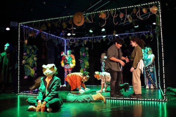 A group of people in masks on a green-lit stage