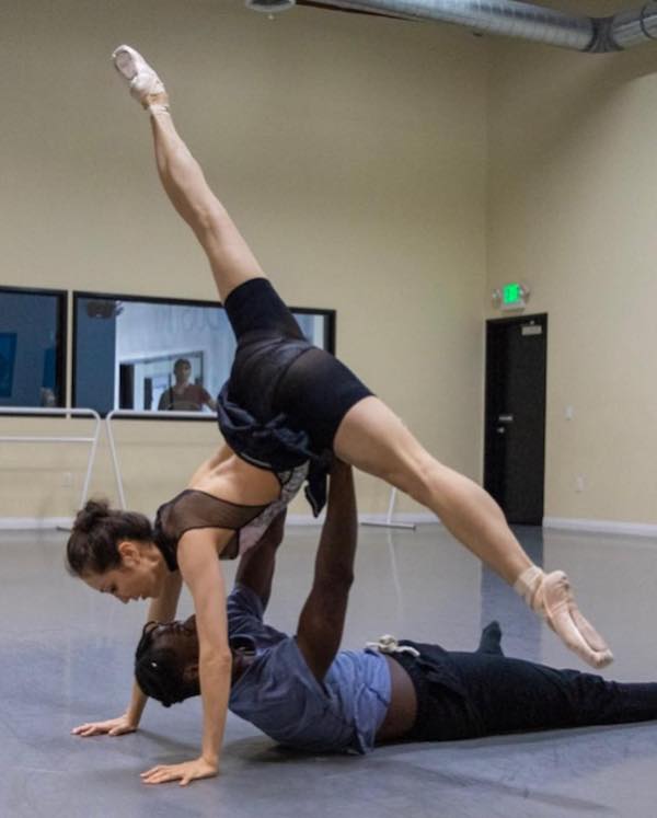 A dancer on the floor lifts a female dancer in the splits