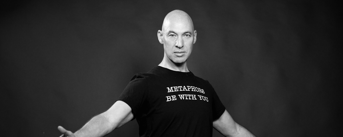 black and white photo of poet Marcus Elman wearing a black t-shirt that reads "Metaphors Be With You".