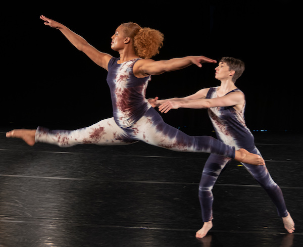 A dancer leaps in front of a second dancer