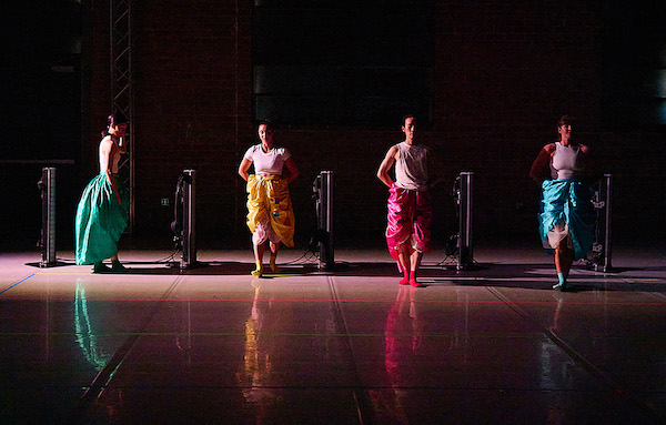 A line of four dancers in different colored skirts