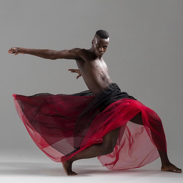 A barechested male dancer in a red sheer skirt