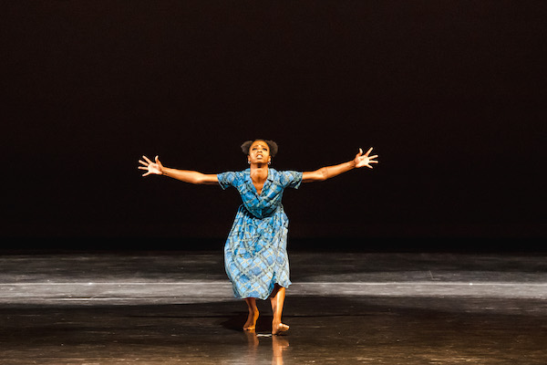 A dancer in blue spreads her arms toward the audience
